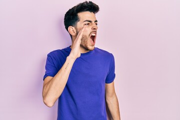 Young hispanic man wearing casual t shirt shouting and screaming loud to side with hand on mouth. communication concept.