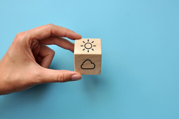 A wooden cube with a picture of the sun and clouds. A symbol of the changeability of the weather and events in life