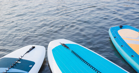 Surf boards on blue clean water surface background. Surfing and SUP boarding equipment in sunset lights close-up. Outdoor water sports. Surfing lifestyle concept.