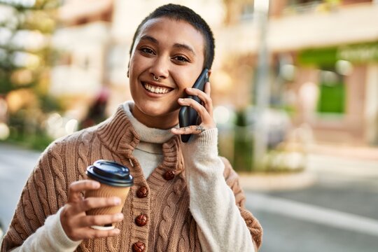 Young hispanic woman with short hair smiling happy drinking a cup of coffee and talking on the phone