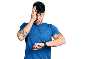Young hispanic man wearing casual t shirt looking at the watch time worried, afraid of getting late