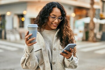 Young latin woman using smartphone and drinking coffee at the city.