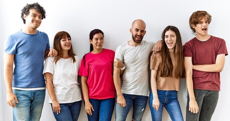Group of young friends standing together over isolated background winking looking at the camera with sexy expression, cheerful and happy face.