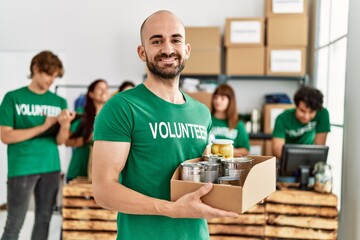 Group of young volunteers working at charity center. Man smiling happy and holding box with food to...
