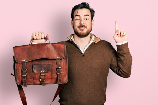 Young hispanic man wearing leather bag smiling with an idea or question pointing finger with happy face, number one