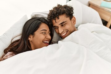 Young latin couple covering with bedsheet lying on the bed at bedroom.