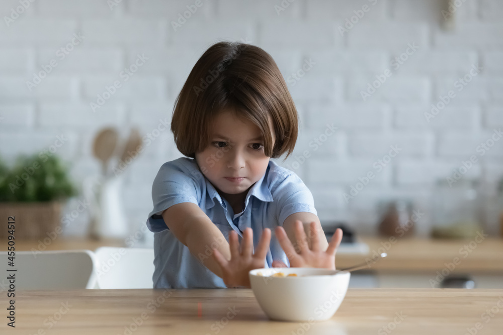 Wall mural stubborn little kid boy rejecting eating dry breakfast corn flakes with milk, sitting in kitchen wit