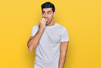 Handsome hispanic man wearing casual white t shirt looking stressed and nervous with hands on mouth biting nails. anxiety problem.