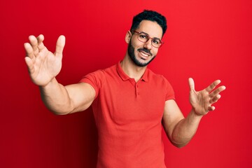 Fototapeta premium Young hispanic man wearing casual clothes and glasses looking at the camera smiling with open arms for hug. cheerful expression embracing happiness.