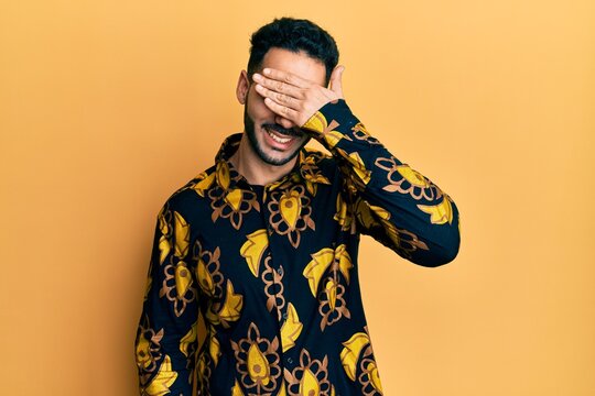 Young hispanic man wearing casual shirt smiling and laughing with hand on face covering eyes for surprise. blind concept.