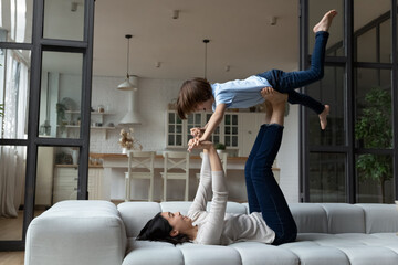 Happy young asian vietnamese mother or babysitter lifting in air laughing cute small child boy,...