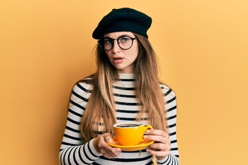 Young caucasian woman wearing french style drinking a cup of coffee clueless and confused expression. doubt concept.