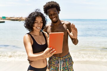 Young interracial tourist couple having video call using touchpad at the beach.