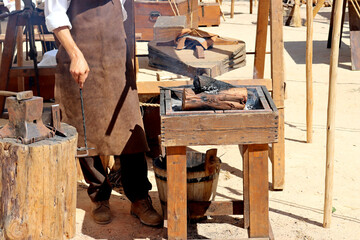  Bellows inflate the fire in the coals. Master Blacksmith in Blacksmith Workshop Demonstrating Old...