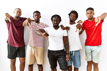 Young african group of friends standing together over isolated background looking unhappy and angry showing rejection and negative with thumbs down gesture. bad expression.