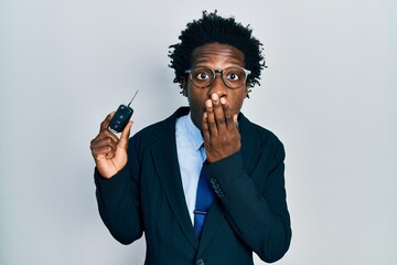 Young african american man holding key of new car covering mouth with hand, shocked and afraid for...