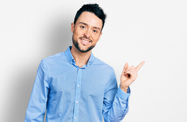 Hispanic man with beard wearing casual business shirt with a big smile on face, pointing with hand and finger to the side looking at the camera.