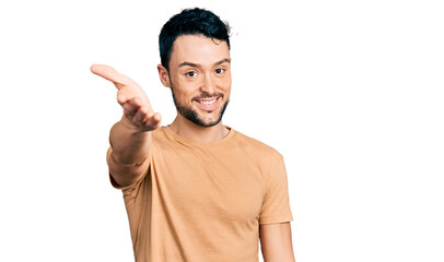 Hispanic man with beard wearing casual t shirt smiling cheerful offering palm hand giving assistance and acceptance.