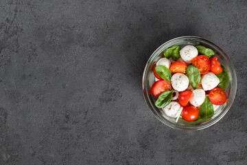 Italian food, Caprese salad of tomatoes, onions, spinach and mozzarella in a glass bowl on a dark gray background top view copy space