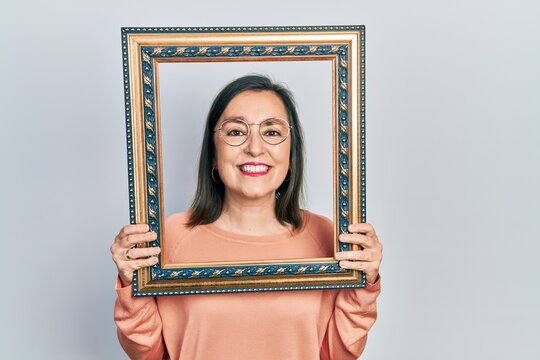 Middle age hispanic woman holding empty frame smiling with a happy and cool smile on face. showing teeth.