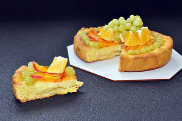 Fruit cake with grapes, peaches and oranges on black background