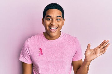 Young handsome hispanic man wearing pink cancer ribbon on shirt celebrating victory with happy...
