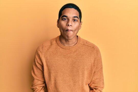 Young handsome hispanic man wearing casual winter sweater making fish face with lips, crazy and comical gesture. funny expression.