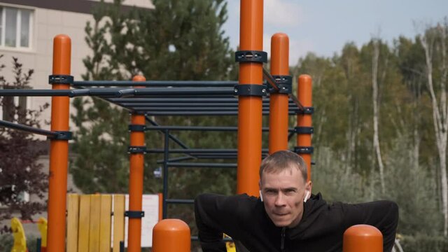 Fit Man Working Out on Parallel Bars Outdoors, Doing Push-ups. Slow Motion. Sport, Fitness, Street Workout and Healthy Lifestyle Concept