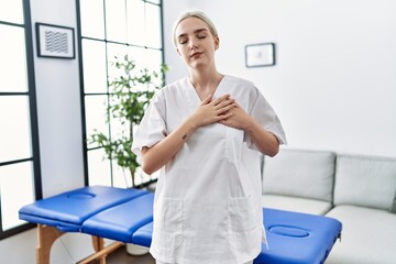 Young caucasian physiotherapy woman working at home smiling with hands on chest with closed eyes and grateful gesture on face. health concept.