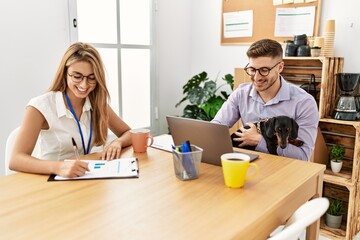 Two business workers smiling happy working with dog at the office.