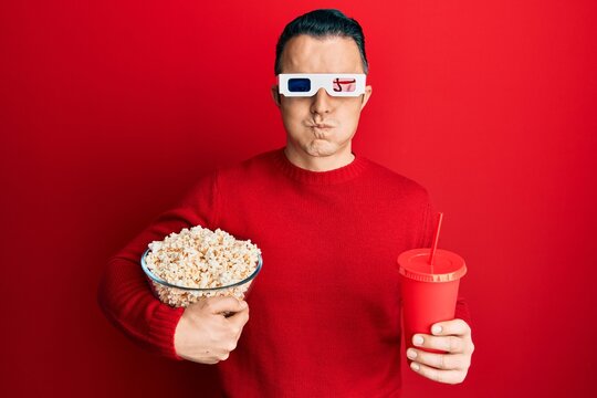 Handsome Young Man Eating Popcorn And Soda Wearing 3d Glasses Puffing Cheeks With Funny Face. Mouth Inflated With Air, Catching Air.