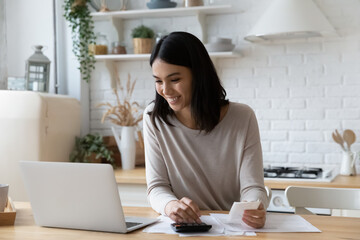 Happy young asian korean woman managing household budget, calculating bills, paying online for...