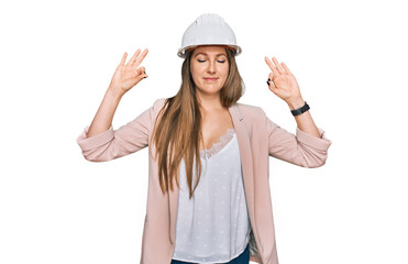 Young blonde woman wearing architect hardhat relax and smiling with eyes closed doing meditation gesture with fingers. yoga concept.