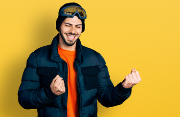 Young hispanic man with beard wearing snow wear and sky glasses excited for success with arms raised and eyes closed celebrating victory smiling. winner concept.