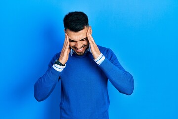 Young hispanic man with beard wearing casual blue sweater with hand on head, headache because stress. suffering migraine.