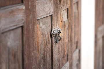 Close-up at aged wooden door which is locked by rusty metal hasp. Vintage style building and background photo. Selective focus at the metal part.
