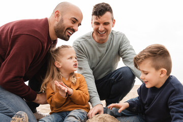 Gay fathers and sons having fun playing together beach - LGBT family love concept - Focus on center...