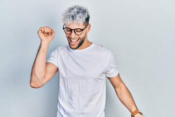 Young hispanic man with modern dyed hair wearing white t shirt and glasses dancing happy and cheerful, smiling moving casual and confident listening to music