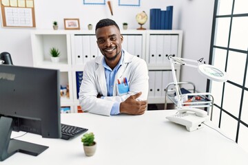 Fototapeta premium Young african doctor man wearing stethoscope at the clinic happy face smiling with crossed arms looking at the camera. positive person.