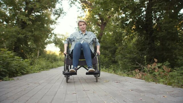 Happy disabled woman is sitting in wheelchair in park, rotation. Concept consequences of car accident and diagnosis of paralysis