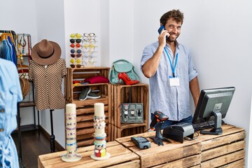 Young hispanic shopkeeper man smiling happy talking on the smartphone working at clothing store.