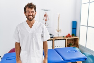 Young handsome physiotherapist man working at pain recovery clinic winking looking at the camera...