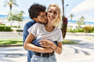 Obraz premium Young beautiful couple of caucasian girlfriend and hispanic boyfriend hugging in love outdoors on a sunny day. Woman and man smiling happy dating relationship