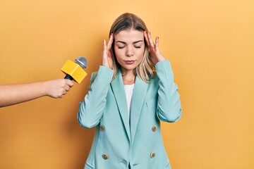 Beautiful caucasian woman being interviewed by reporter holding microphone suffering from headache...