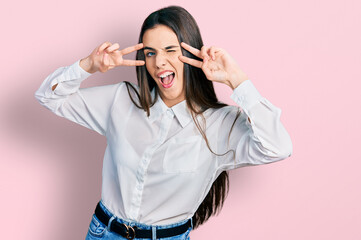 Young brunette teenager doing peace gesture close to eyes winking looking at the camera with sexy...