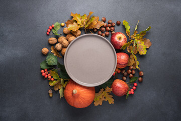 Obraz na płótnie Canvas Empty plate surrounded by autumn decor. Autumn Thanksgiving table with pumpkin, apples, nuts and bright leaves. Dark background, top view