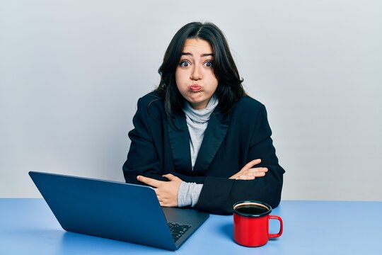 Beautiful Hispanic Business Woman With Arms Crossed Gesture At The Office Puffing Cheeks With Funny Face. Mouth Inflated With Air, Catching Air.