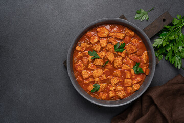 Stew turkey or chicken meat in tomato sauce. Meat dish in frying pan on black background