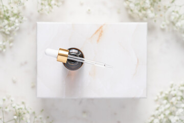 Cosmetic bottle with pipette on marble box. Marble background with white gypsophila flowers....