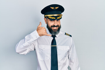 Young hispanic man wearing airplane pilot uniform smiling doing phone gesture with hand and fingers like talking on the telephone. communicating concepts.